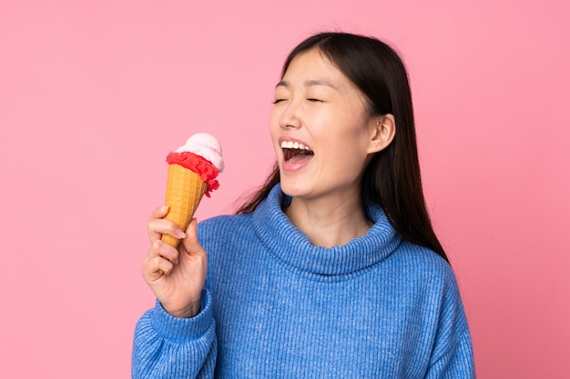 Young asian woman with a cornet ice cream on pink wall