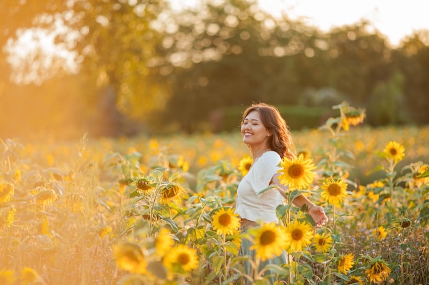 Young Asian woman with curly hair in a field of sunflowers at sunset.