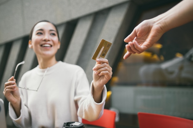 写真 手で眼鏡をかけた若いアジアの女性はコーヒーショップやお茶やコーヒーの支払いとラップトップを使用して外に座っています。