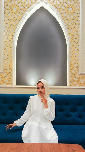 Young Asian woman with a graceful smile hands holding a sofa and hijab sitting on a sofa with a back