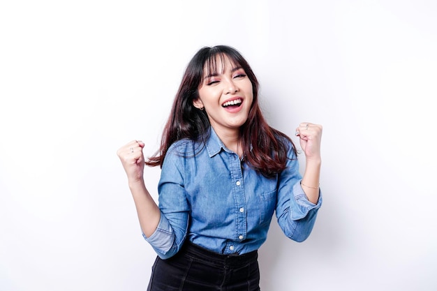 A young Asian woman with a happy successful expression wearing blue shirt isolated by white background