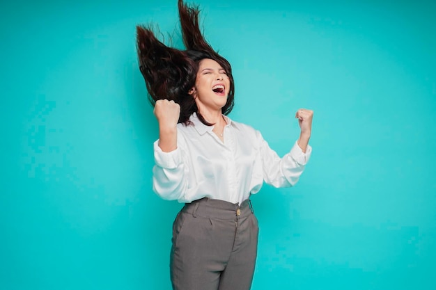 A young Asian woman with a happy successful expression wearing white shirt isolated by blue background