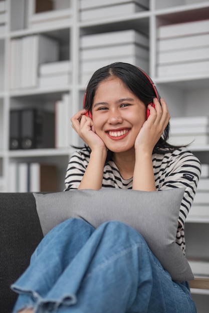 Young asian woman with headphones relaxing at home listening to music sitting on cozy sofa wearing headphone