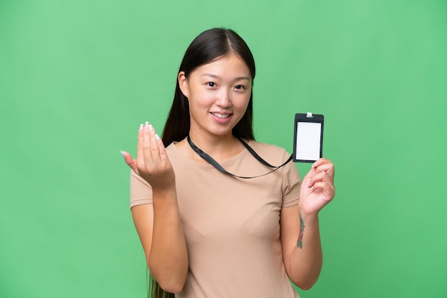 Young asian woman with id card over isolated background\
inviting to come with hand happy that you came