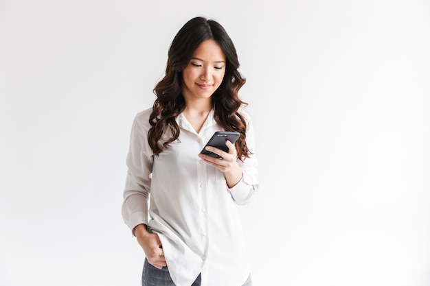 Young asian woman with long dark hair holding and using black mobile phone