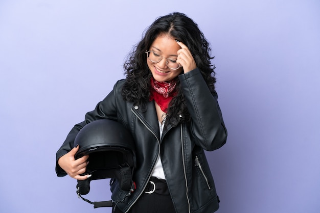 보라색 배경에 오토바이 헬멧을 쓴 젊은 아시아 여성이 웃고 있다
