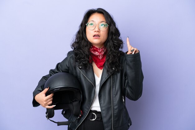 Young asian woman with a motorcycle helmet isolated on purple background thinking an idea pointing the finger up