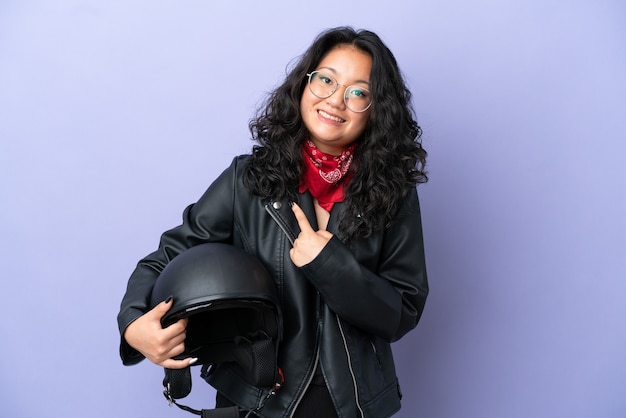 Young asian woman with a motorcycle helmet isolated on purple background with surprise facial expression