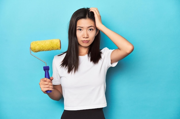 Young Asian woman with paint roller DIY concept being shocked she has remembered important meeting