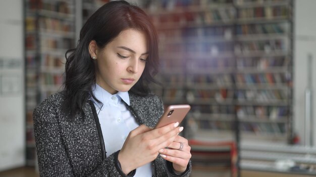 写真 本棚のレンズフレアの背景に携帯電話を持つ若いアジア女性