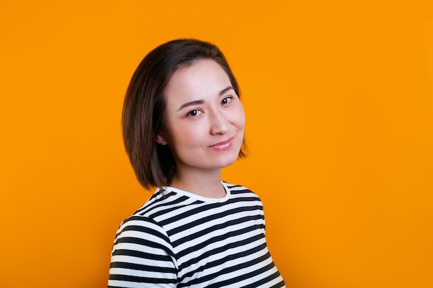 Young asian woman with pleasant friendly smil wears casual strioed sweater stands alone against yellow background