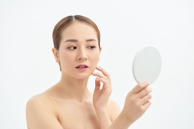 Young Asian woman with problem face looking at the mirror  over white background.