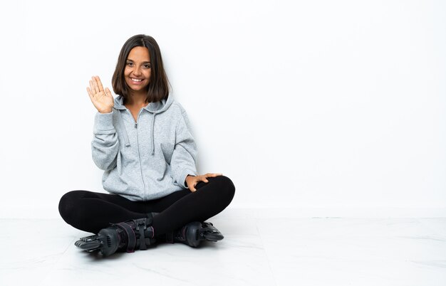 Young asian woman with roller skates on the floor saluting with hand with happy expression