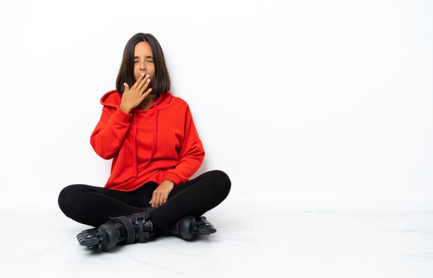 Young asian woman with roller skates on the floor yawning and coning wide open mouth with hand