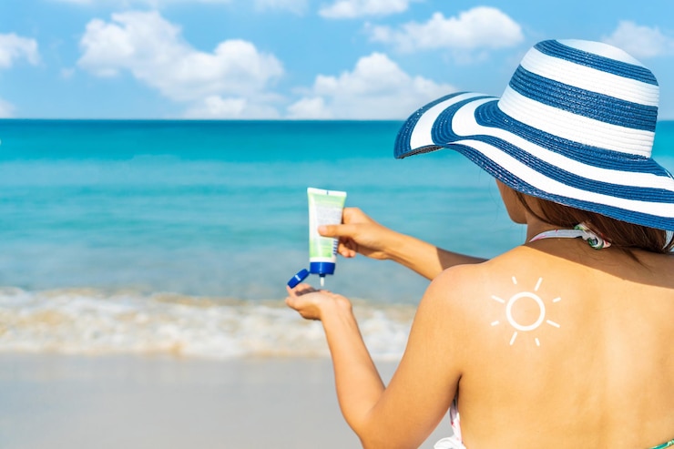 Photo young asian woman with sun shape on the shoulder apply sun cream on to her hand summer on beach concept