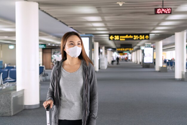 空港ターミナルで歩いてサージカルマスク顔保護を持つ若いアジア女性。医療と保護の概念。