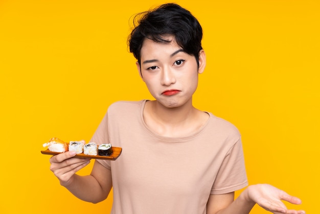 Young Asian woman with sushi making doubts gesture while lifting the shoulders