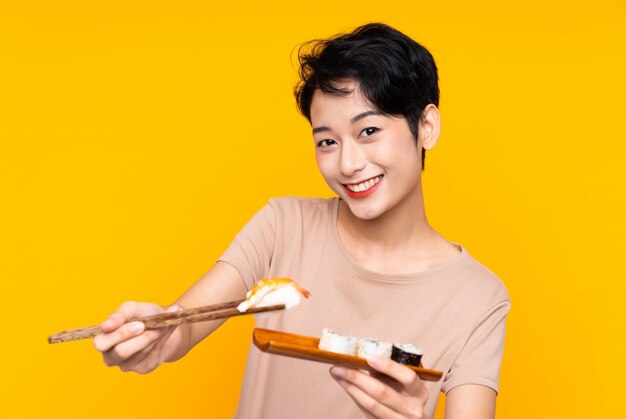 Young Asian woman with sushi over yellow background