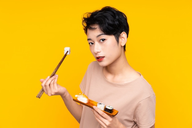 Young Asian woman with sushi over yellow background