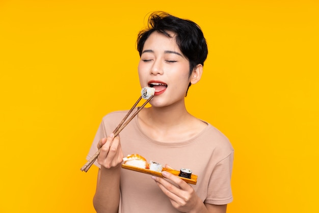 Young Asian woman with sushi over yellow background