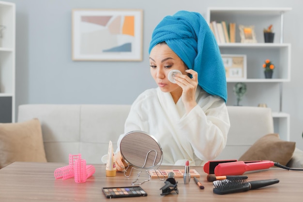 Young asian woman with towel on her head sitting at the dressing table at home cleaning face using cotton pad doing morning makeup routine