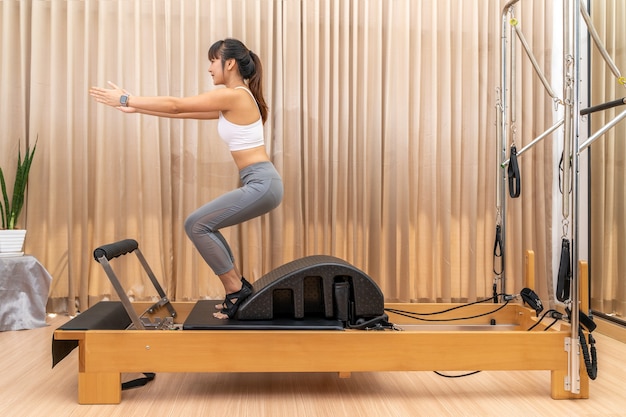 Giovane donna asiatica che lavora sulla macchina del riformatore di pilates durante la sua formazione esercizio di salute