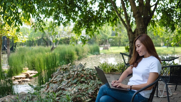 公園に座ってノートパソコンのキーボードで作業し、入力している若いアジア人女性