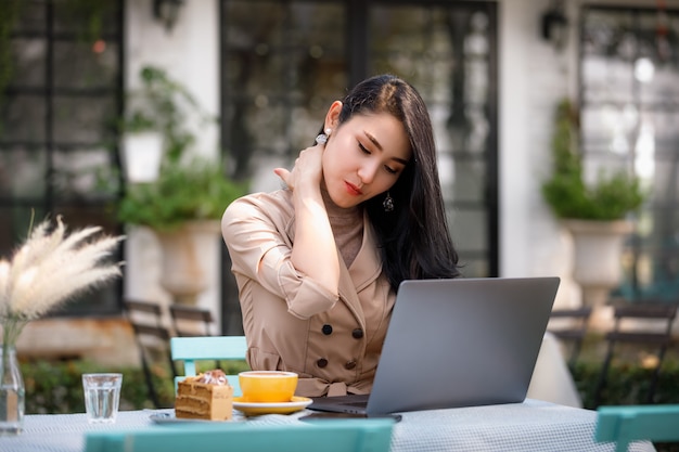 庭でラップトップコンピューターでの作業と首の痛みを持つ若いアジア女性