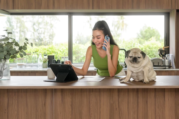 Young asian woman working with tablet and enjoying with her dog in the kitchen at home