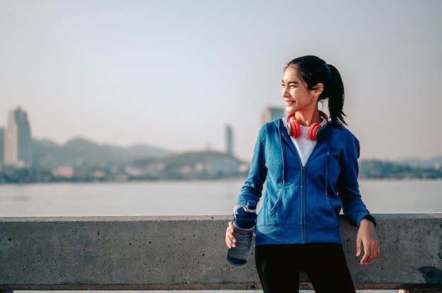 Young asian women drink water and stand to rest after jogging a morning workout in the city A city that lives healthy in the capital Exercise fitness jogging running lifestyle healthy concept