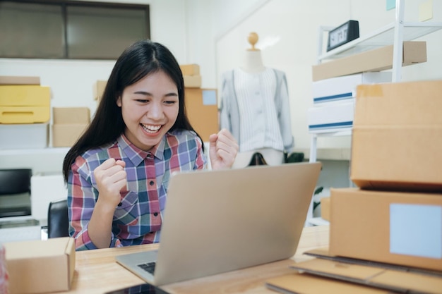 顧客からの新しい注文の後に幸せな若いアジアの女性。彼のオンラインストアの大売り出しでアジアの女性が成功したことの驚きと衝撃的な顔。オンライン販売。オンラインショッピング。