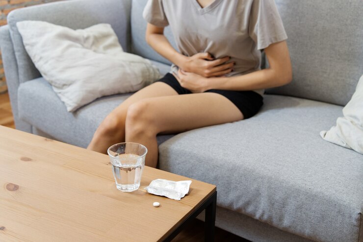 腹痛に苦しんでいるソファの上の若いアジア女性。