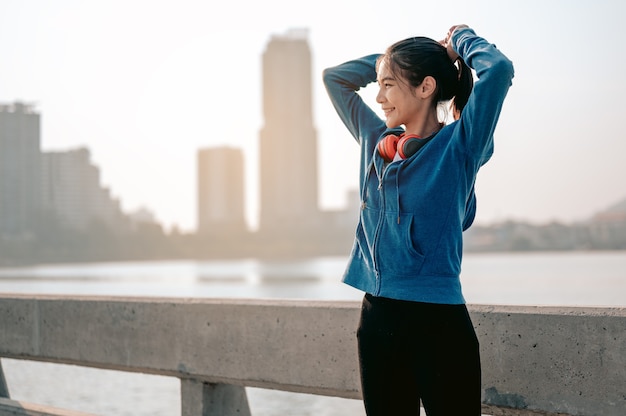 若いアジアの女性は、都市のランニングでの朝の運動の準備のために髪を結んだ