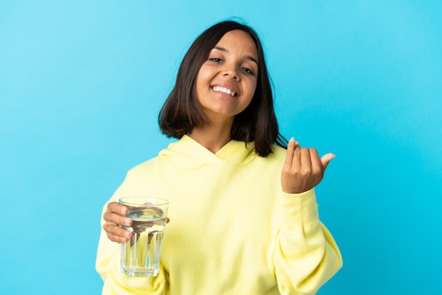 Young asiatic woman with a glass of water isolated on blue inviting to come with hand