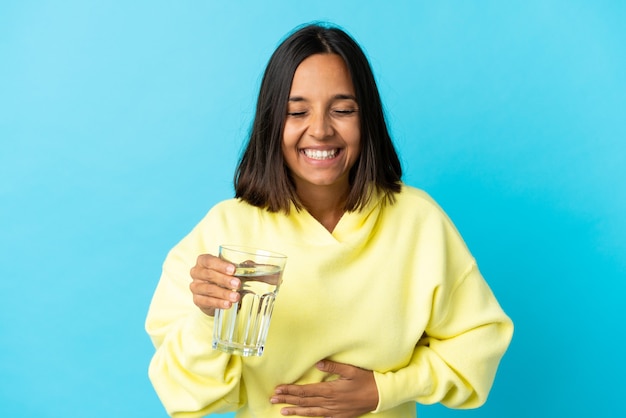 Photo young asiatic woman with a glass of water isolated on blue smiling a lot