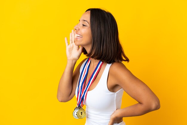 Young asiatic woman with medals isolated on white wall shouting with mouth wide open to the side