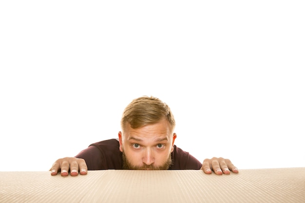 Young astonished man opening the biggest postal package isolated on white. Shocked male model on top of cardboard box