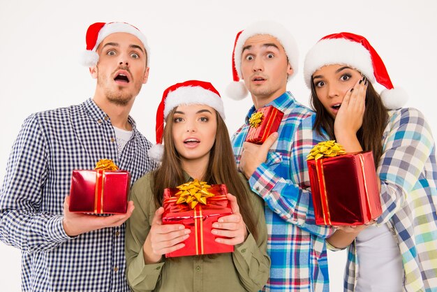 Young astonished people in Santa hats holding presents