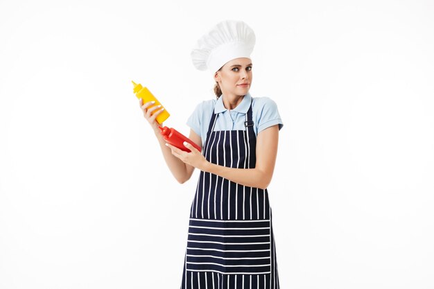 Young astonished woman chef in striped apron and white hat thoughtfully 