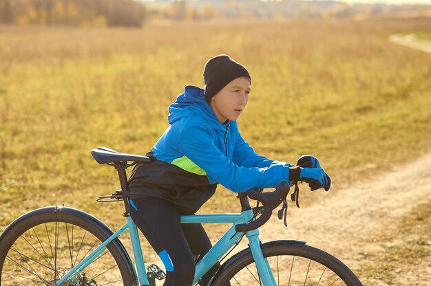 Foto un giovane atleta su una bici sportiva blu si siede su una bicicletta sullo sfondo di una strada di campo.