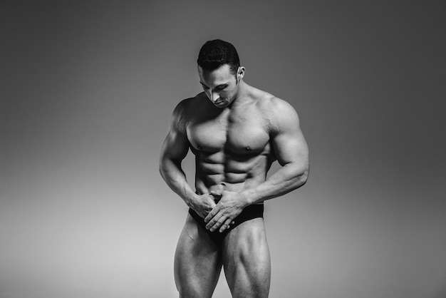 A young athlete bodybuilder poses in the studio topless, showing off his abs and muscles