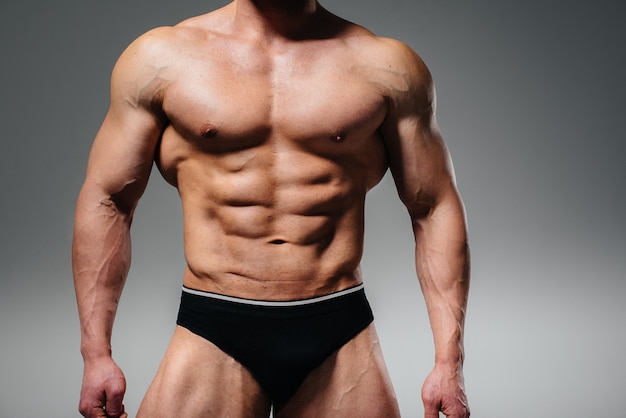 A young athlete bodybuilder poses in the studio topless, showing off his abs and muscles