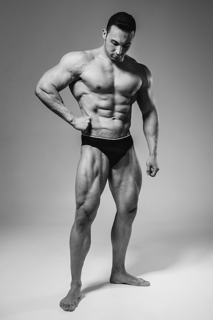 A young athlete bodybuilder poses in the studio topless, showing off his abs and muscles