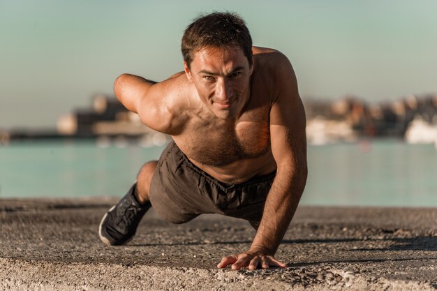 Young athlete does push-ups on one arm in the early morning.