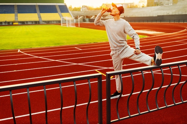 Молодой спортсмен делает растяжку перед бегом на стадионе Фото высокого качества