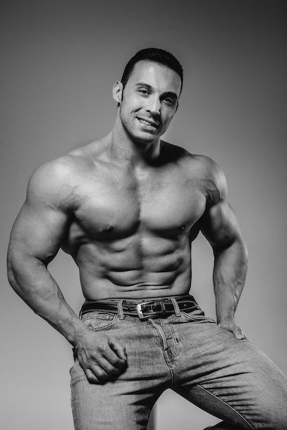 A young athlete in jeans poses sitting in the studio. Black and white.