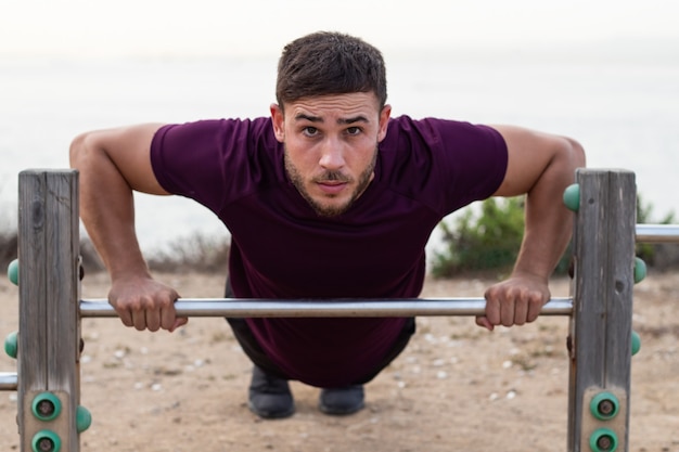 Foto uomo giovane atleta facendo flessioni su un bar all'aperto