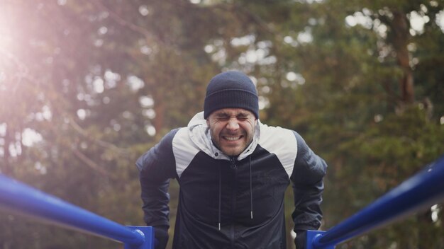 Photo young athlete man doing pushups exercise on bars in winter park outdoors