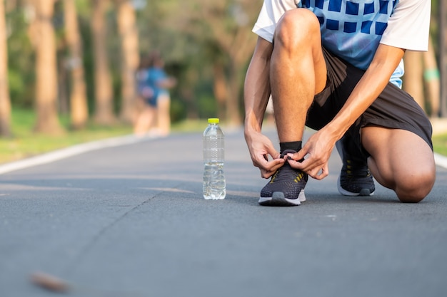 Young athlete man tying running shoes in the park outdoor. 