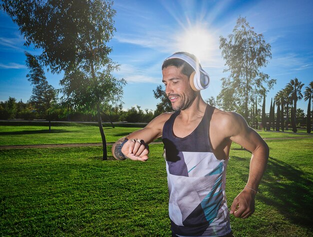 Il corridore giovane atleta che indossa i caschi sorride mentre guarda il cardiofrequenzimetro durante l'allenamento nel parco